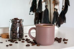 A ceramic mug of black coffee beside roasted coffee beans on a wooden table.