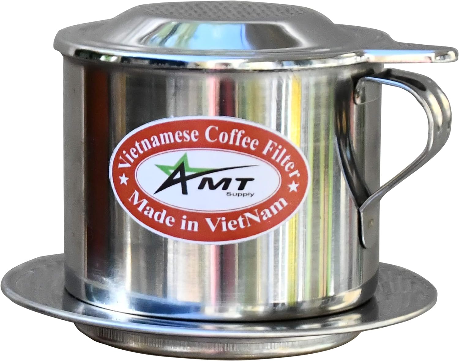 Stainless Vietnamese phin filter resting on a white cup of condensed milk beside an iced coffee and ground coffee.