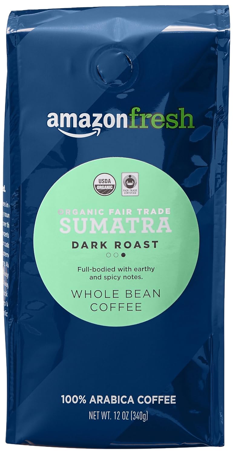Teak bowl of oily dark roast Sumatra beans beside a black mug of coffee, spices and a banana leaf.
