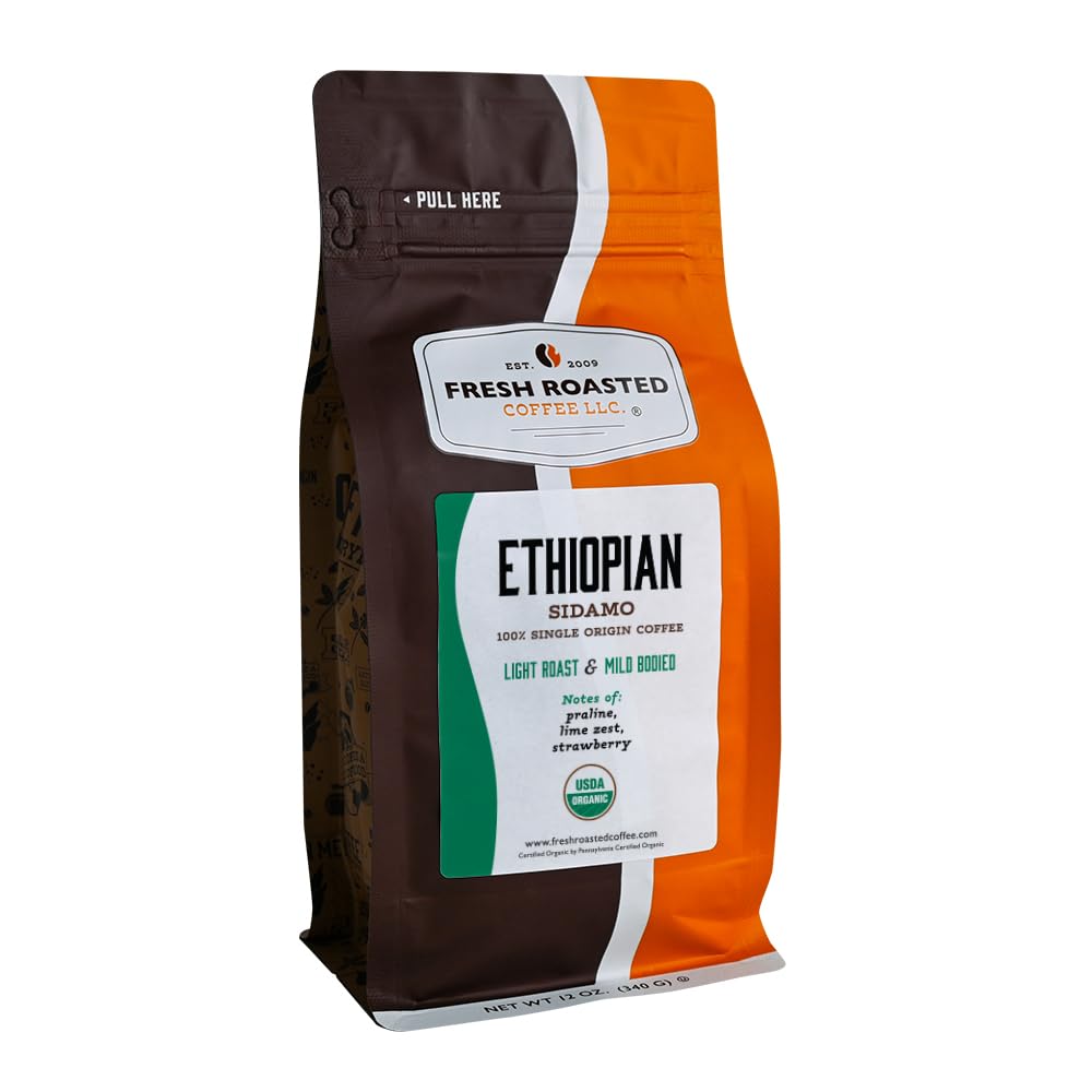A white pour-over cup of black coffee stacked on a mug beside roasted beans, blueberries, a halved apricot, and jasmine blossoms on linen, illustrating a fruity Ethiopian natural coffee to drink black.